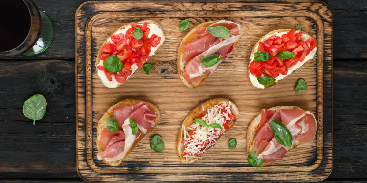set of small sandwiches with prosciutto, tomatoes, parmesan cheese, fresh basil served on wooden board with glass of wine, top view set of small sandwiches with prosciutto, tomatoes, parmesan cheese, fresh basil served on wooden board with glass of wine, top view