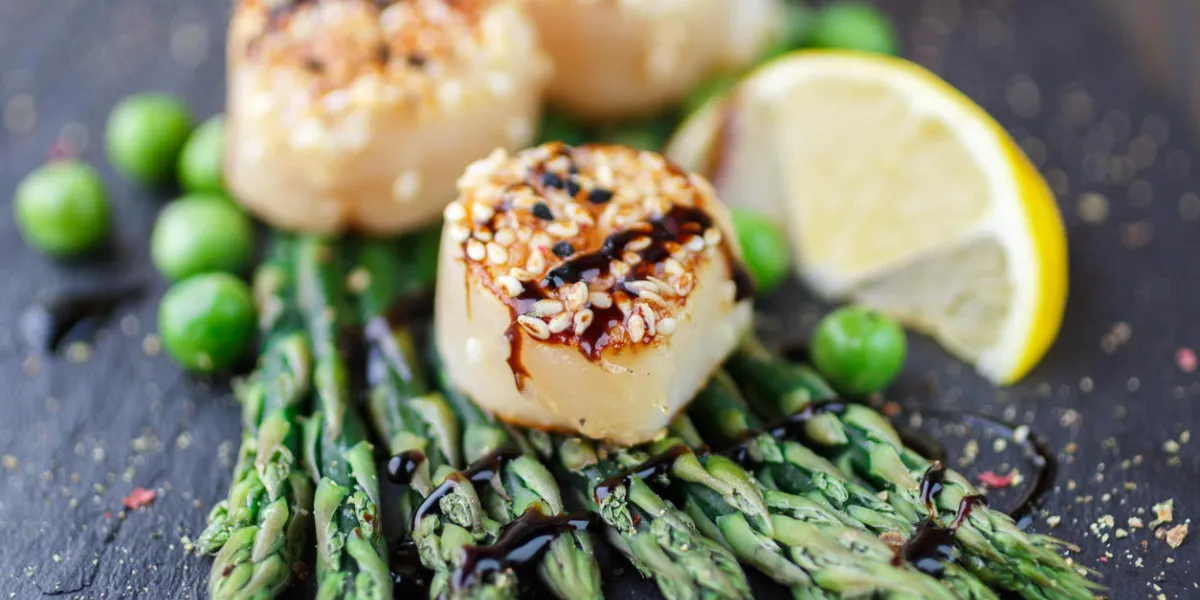 pétoncle frit aux graines de sésame et sauce balsamique, asperges, citron et pois verts sur une plaque noire peu profonde pétoncle frit aux graines de sésame et sauce balsamique, asperges, citron et pois verts sur une plaque noire peu profonde