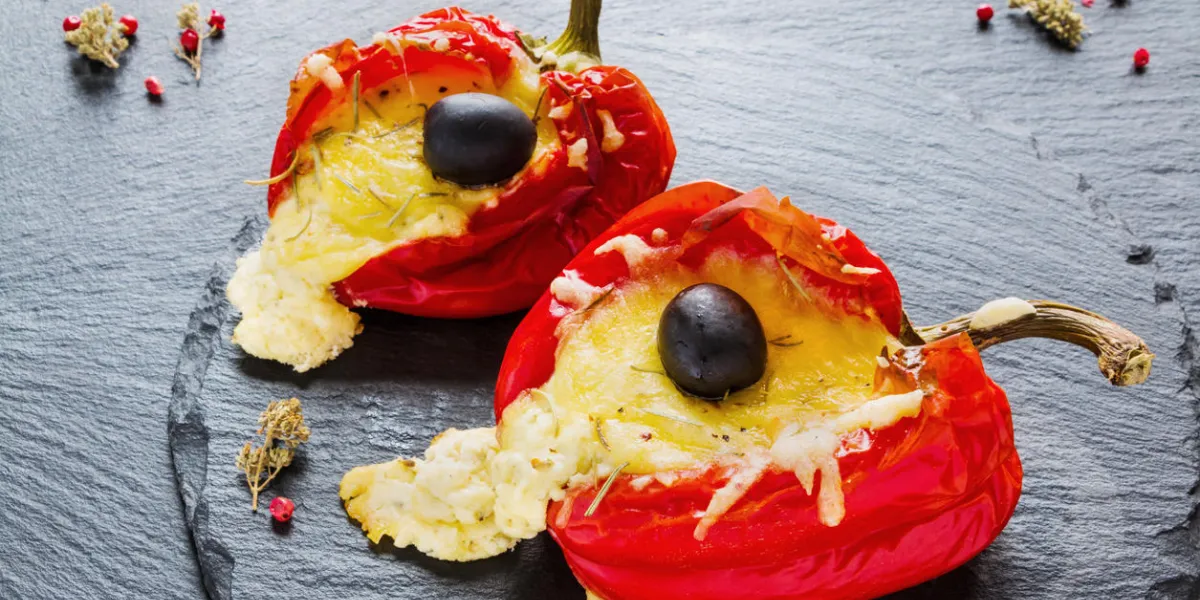 stuffed red sweet peppers with feta cheese and olives on black stone background