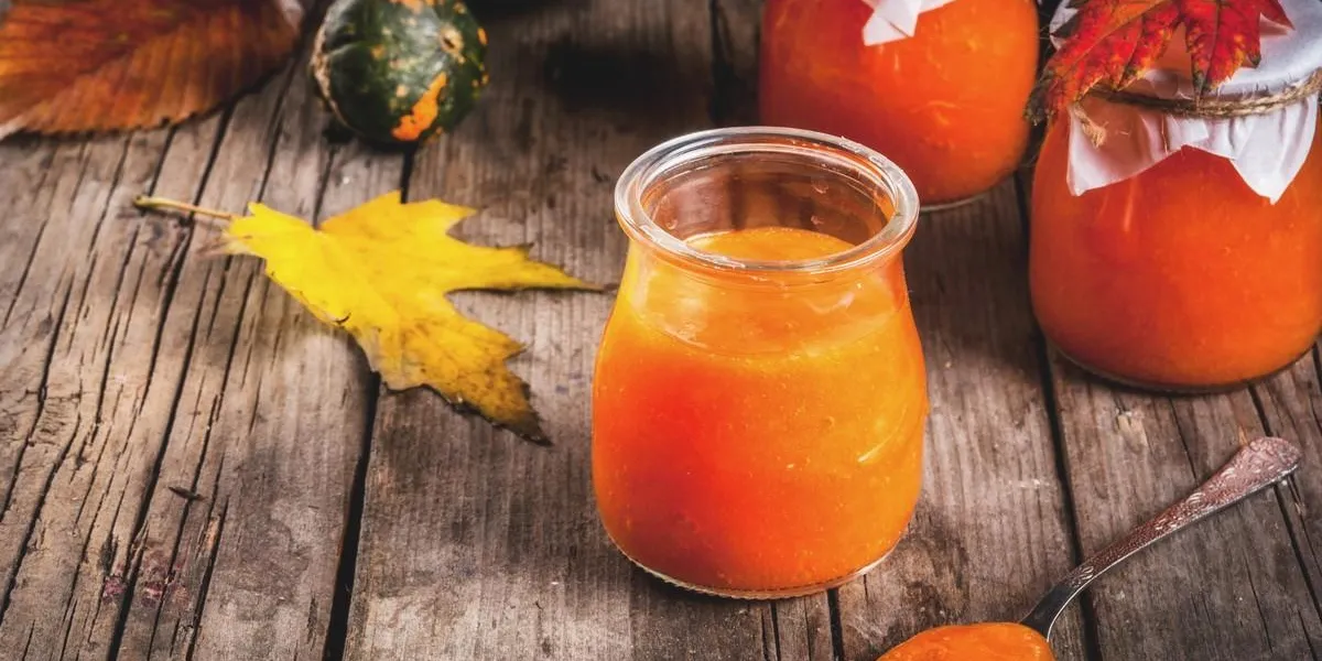 autumn recipes, dishes from a pumpkin sweet spicy pumpkin jam in a serving jar, with a spoon, on an old rustic wooden table decorated with pumpkins, autumn leaves, a blanketcopy space