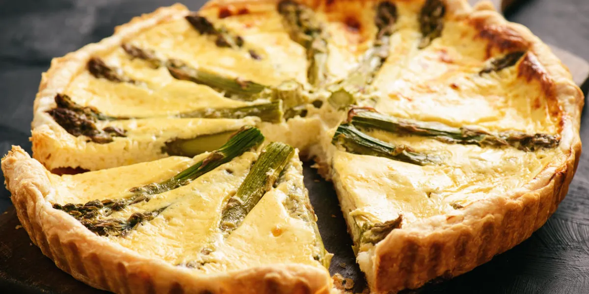 homemade tart with asparagus and cheese on black background
