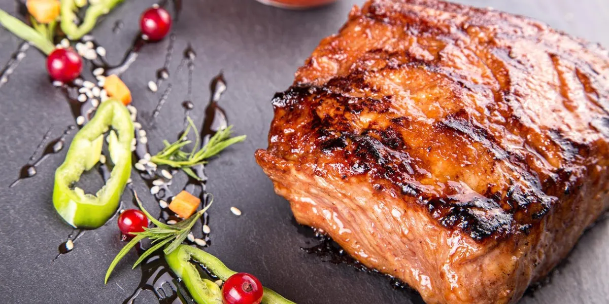 steak sur ardoise debout à côté d'une saucière avec du ketchup sur le tableau est le piment, les carottes en dés, les groseilles rouges, le sésame