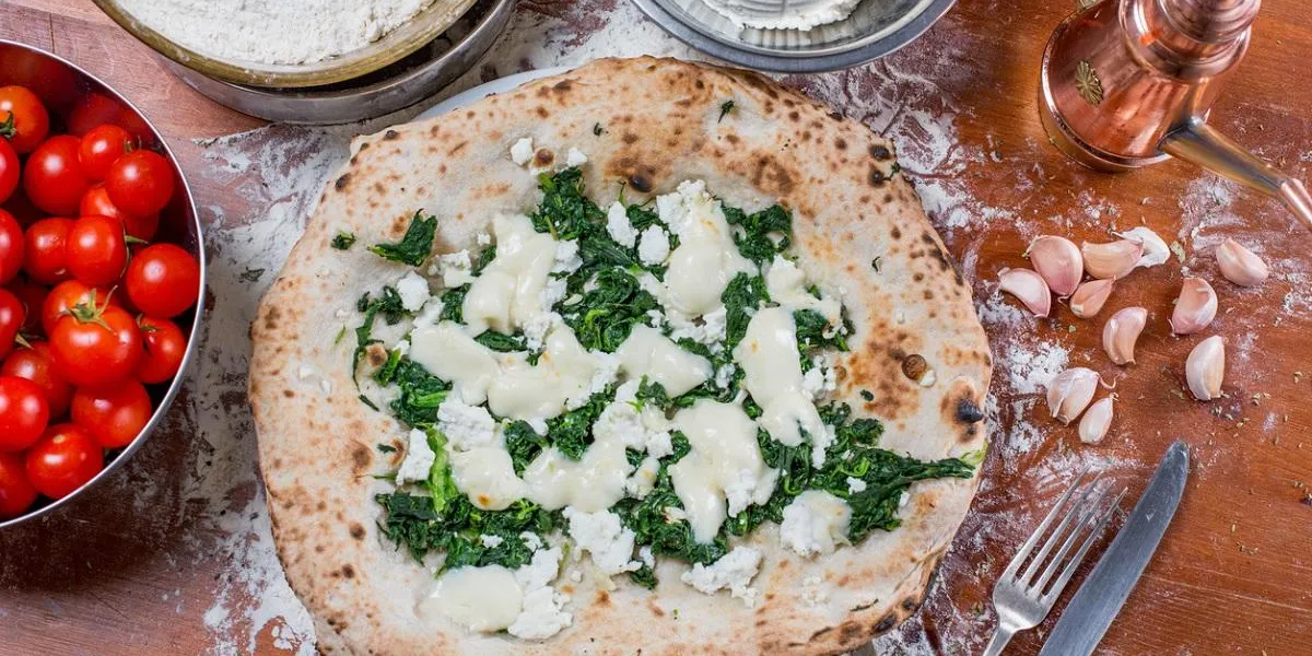 traditional italian pizza with mozzarella cheese, ricotta and spinach with fresh tomatos, on a wooden table