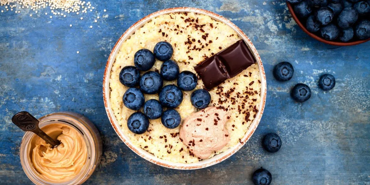 bol de petit déjeuner de porridge sans gluten amaranth et quinoa avec bleuets et chocolat sur fond bleu cru vue de dessus, frais généraux, espace copie plat bol de petit déjeuner de porridge sans gluten amaranth et quinoa avec bleuets et chocolat sur fond bleu cru vue de dessus, frais généraux, espace copie plat