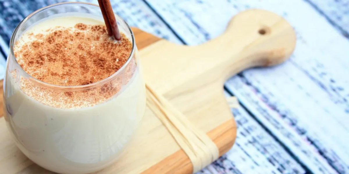 lait de poule dans un petit verre avec un bâton de cannelle à l'intérieur avec de la cannelle sur le dessus d'une planche de bois sur un fond en bois rustique gris